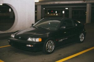 Vintage black Honda CR-X parked in dimly lit parking garage. Urban night setting.